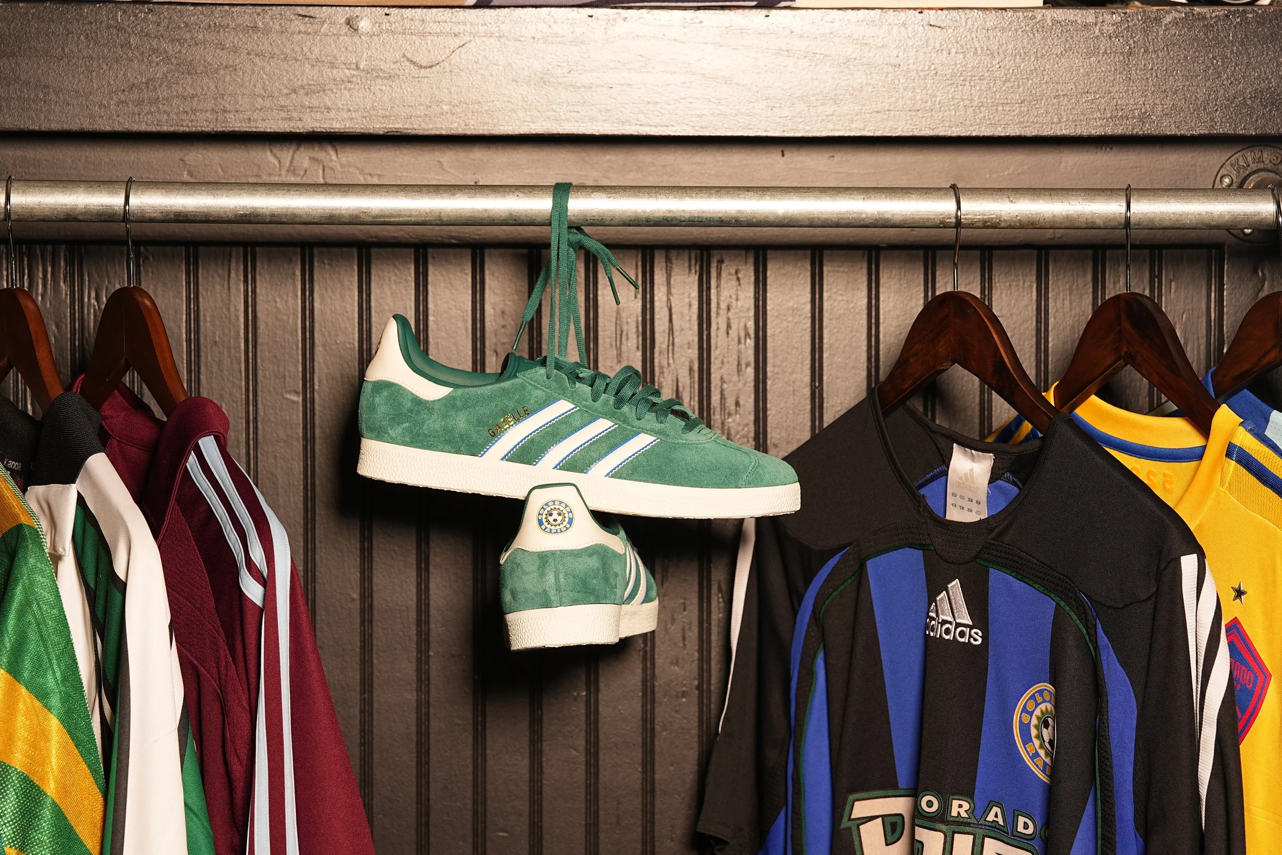 A closet rack with sports jerseys and sneakers, including an Adidas shoe hanging from a hook.