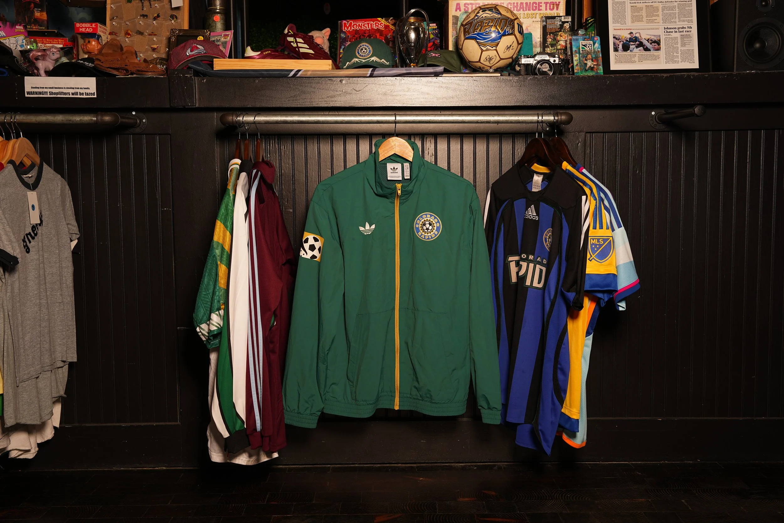 Hanging soccer jackets and jerseys in a store, with various sports memorabilia on shelves above.