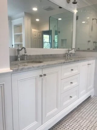 Bathroom vanity with double sinks, marble countertop, large mirror, and white cabinetry