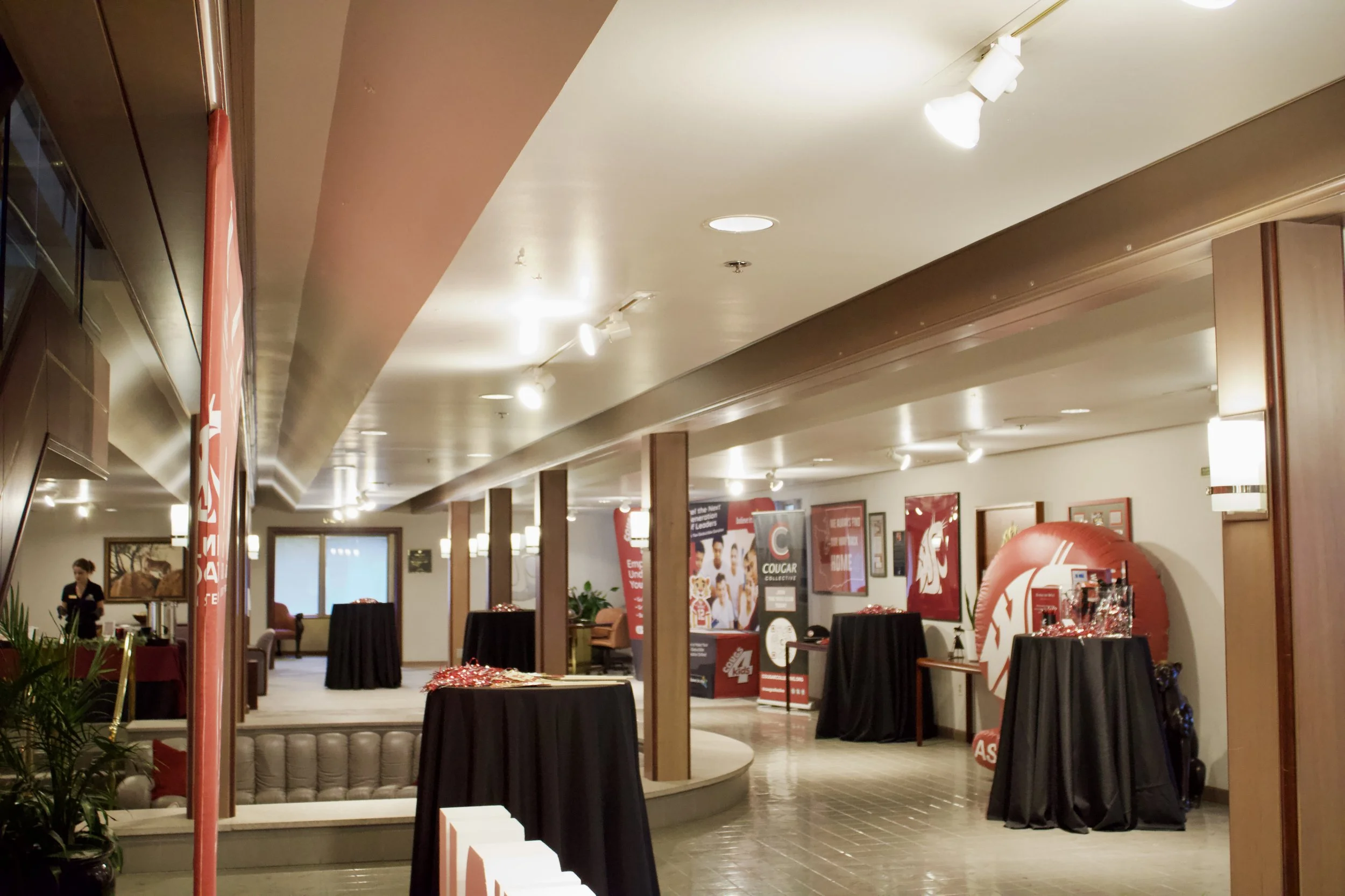 Interior view of a room decorated with sports team banners, tables covered with black cloths, and promotional displays, likely at a corporate or event space.