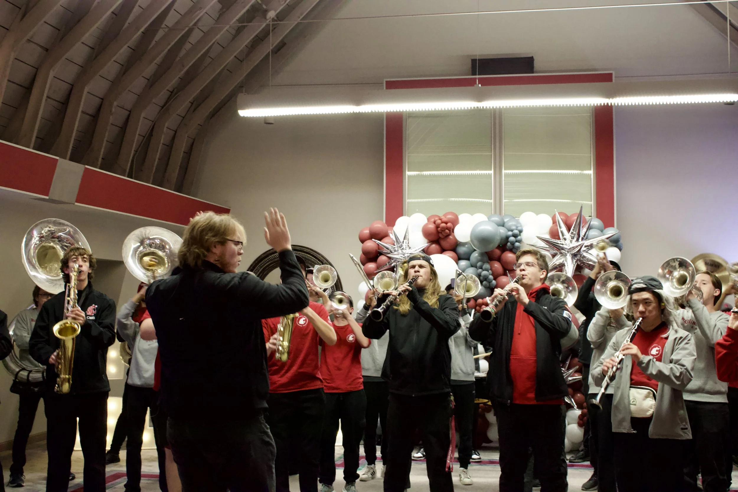A group of people playing brass instruments and clarinets at an indoor event with balloon decorations in the background.