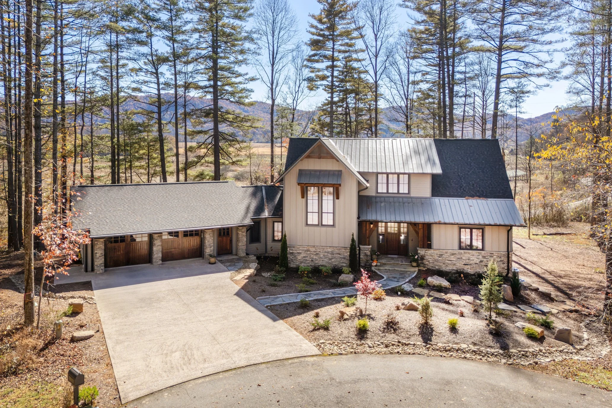 A large modern house with a stone and siding exterior, metal roof, and attached garage, surrounded by trees and a landscaped yard.