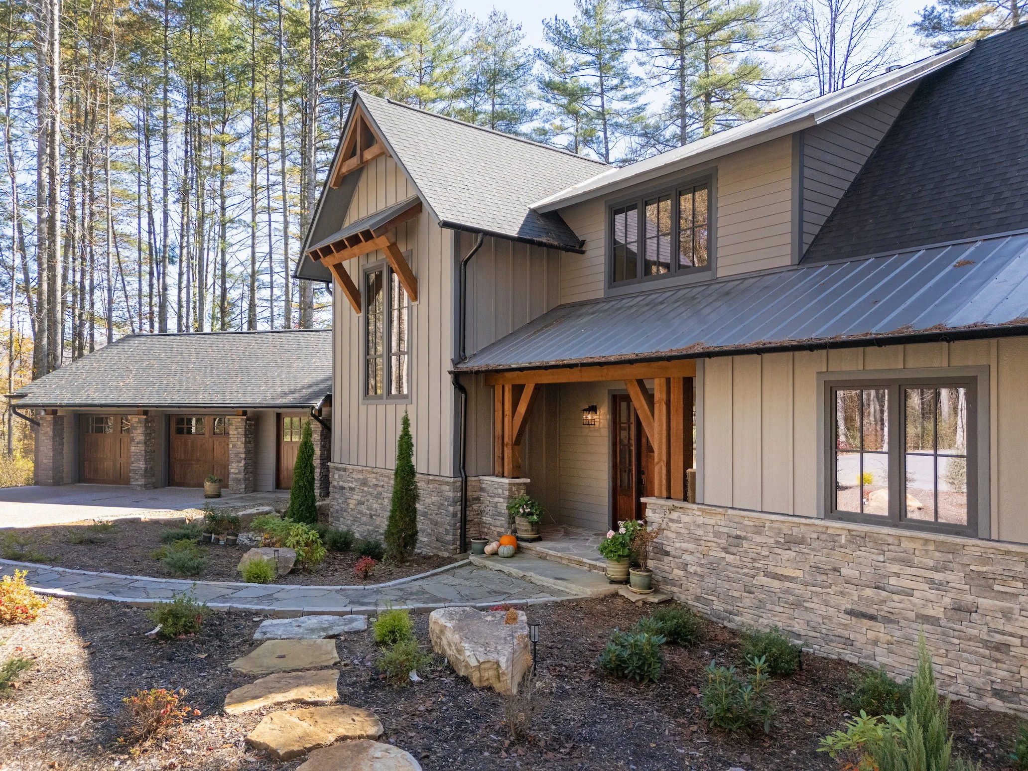 Modern house with stone and wood exterior, surrounded by a landscaped garden with small bushes and trees, featuring a stone pathway leading to the front entrance.