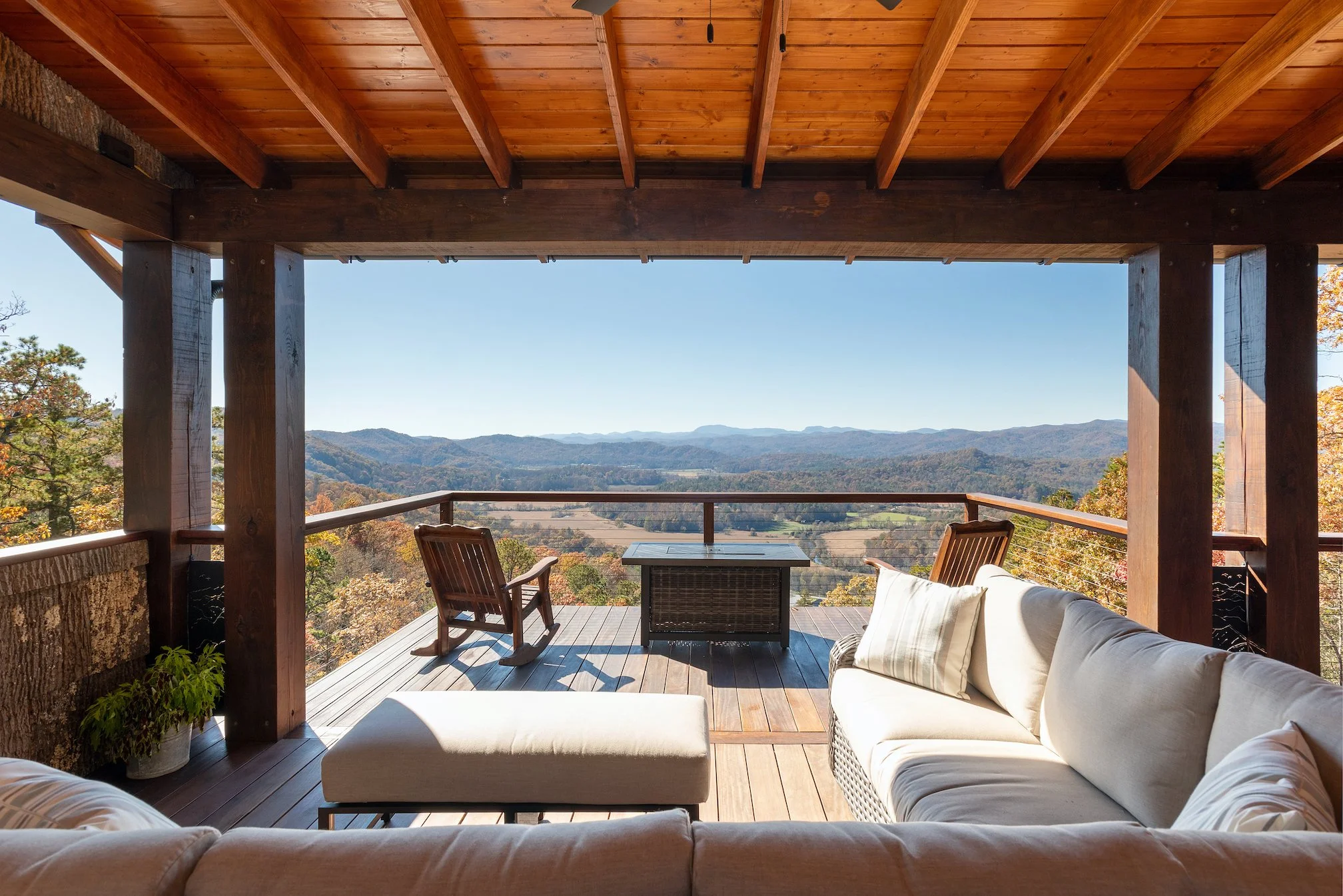 View of a wooden balcony with outdoor furniture overlooking a mountain landscape on a clear day.