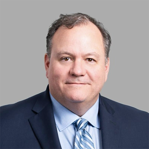 Portrait of Matt Fifield, Chairman, in a navy suit and blue tie, sitting in a modern office.