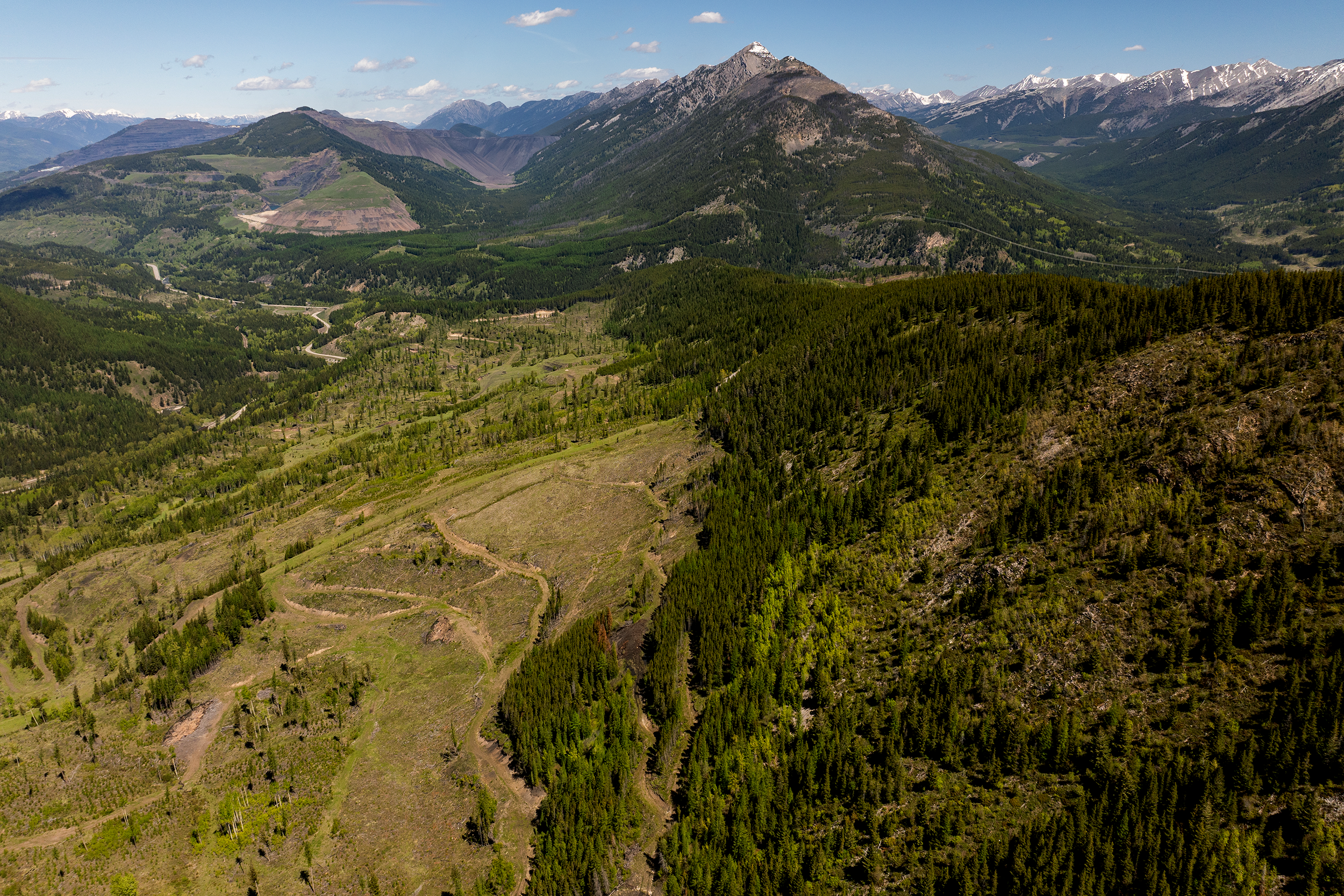 Aerial view of the project site mountainous landscape with lush green trees, winding roads, and snow-capped peaks under a partly cloudy sky.