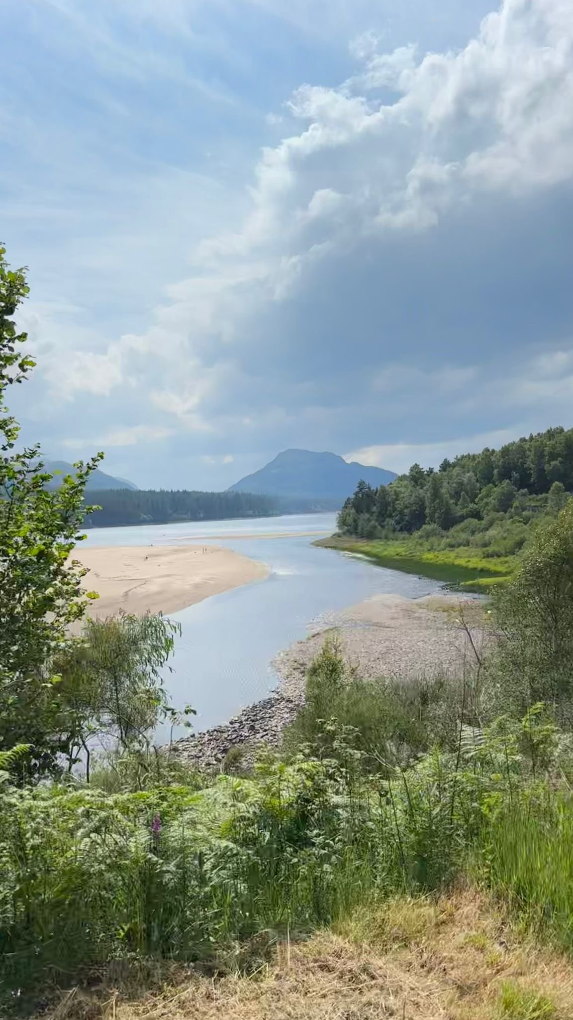 A scenic landscape of a river winding through lush green terrain with mountains in the distance under a partly cloudy sky.