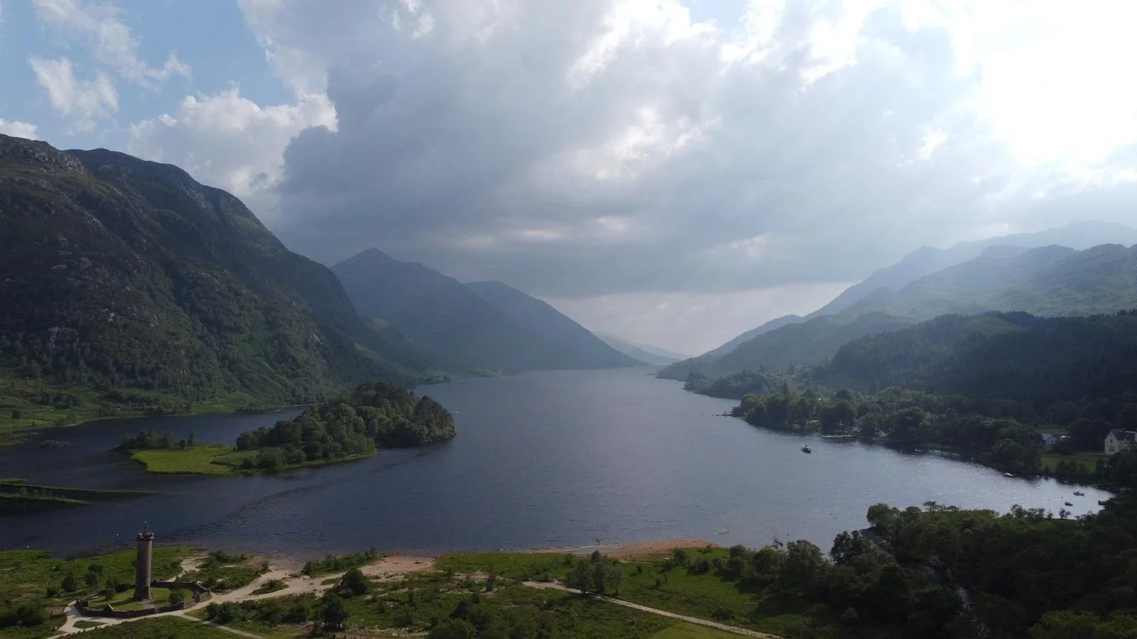 Scenic view of a river flowing through a valley surrounded by green mountains on a cloudy day.