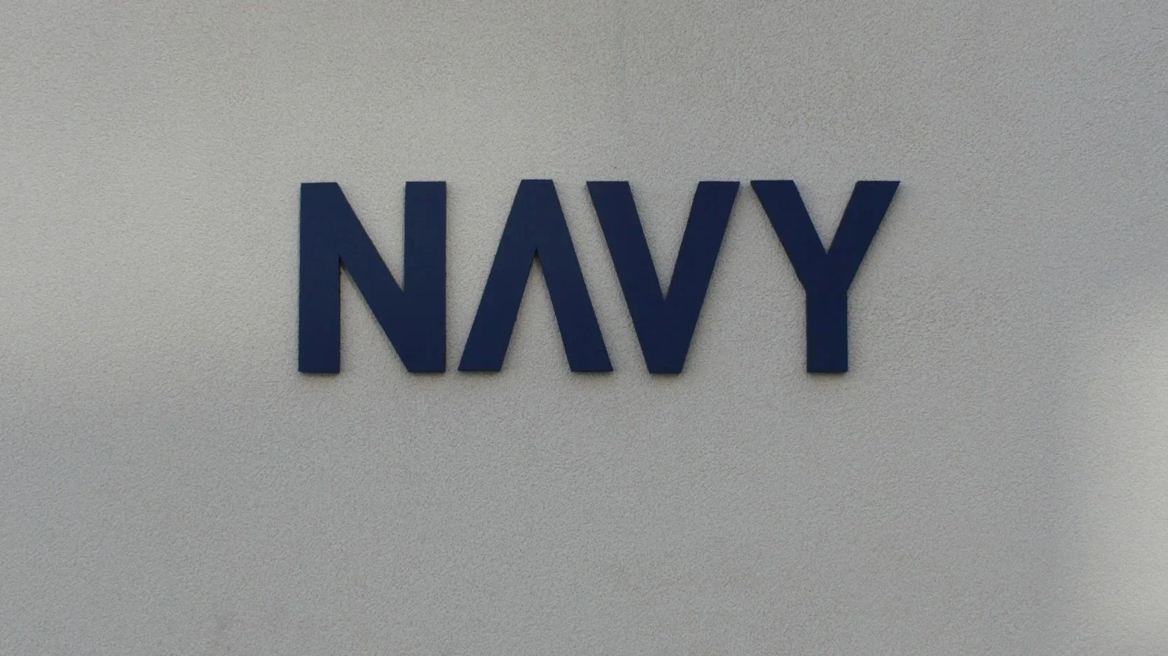 Blue 3D letters spelling 'NAVY' on a textured white wall.