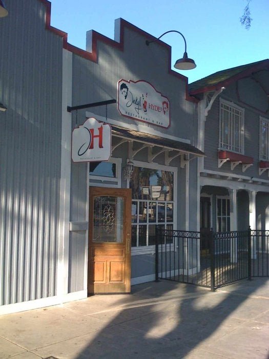 Street view of a building with a restaurant sign, a wooden door with decorative glass, and a metal railing outside, during daytime.