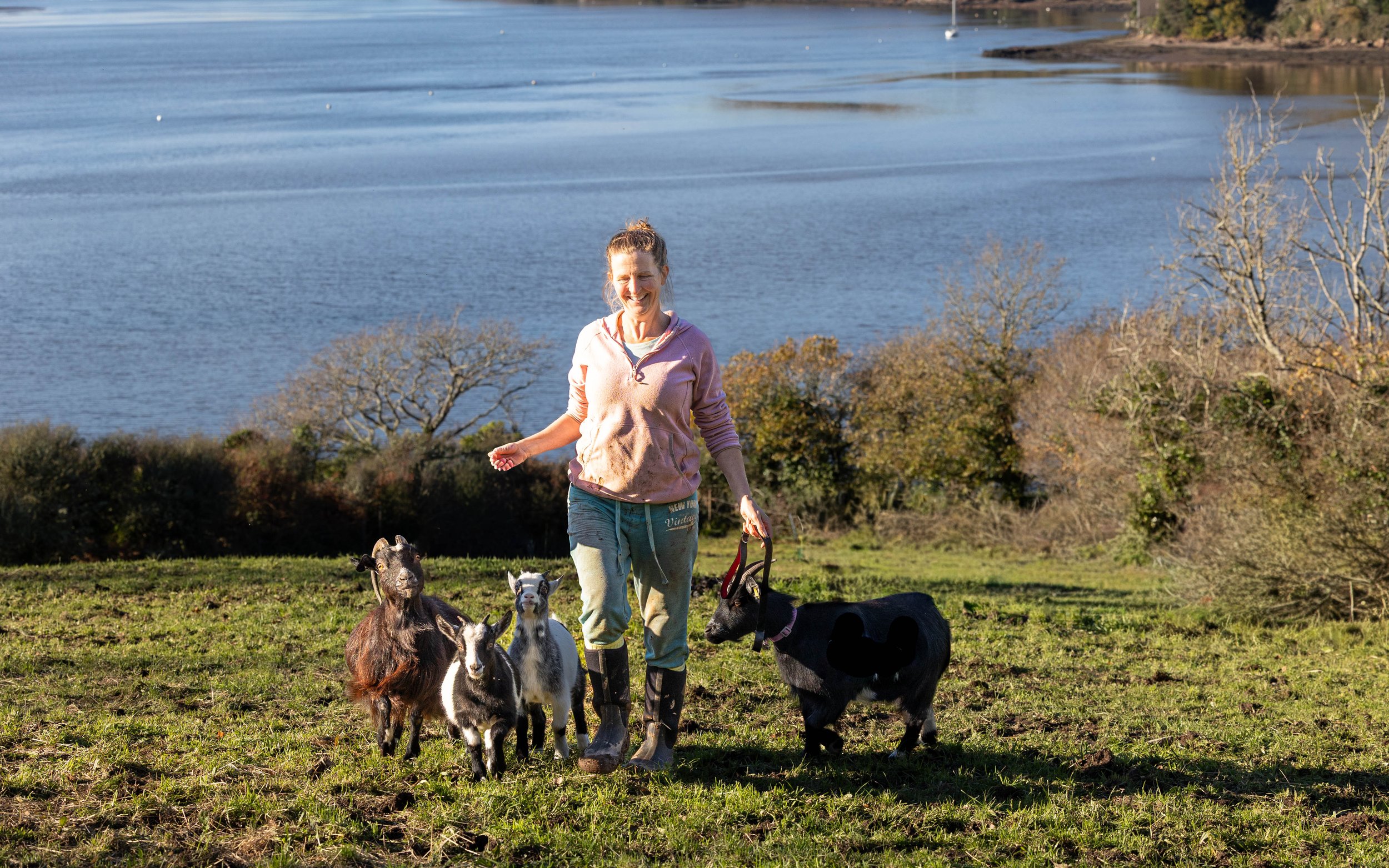 A woman walking four goats near a river.