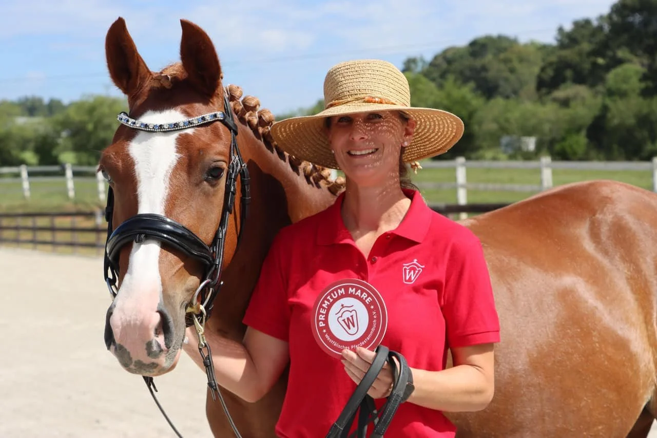 Katharina Huenermann standing next to a chestnut Welsh pony with a white blaze, holding a red and white ribbon.