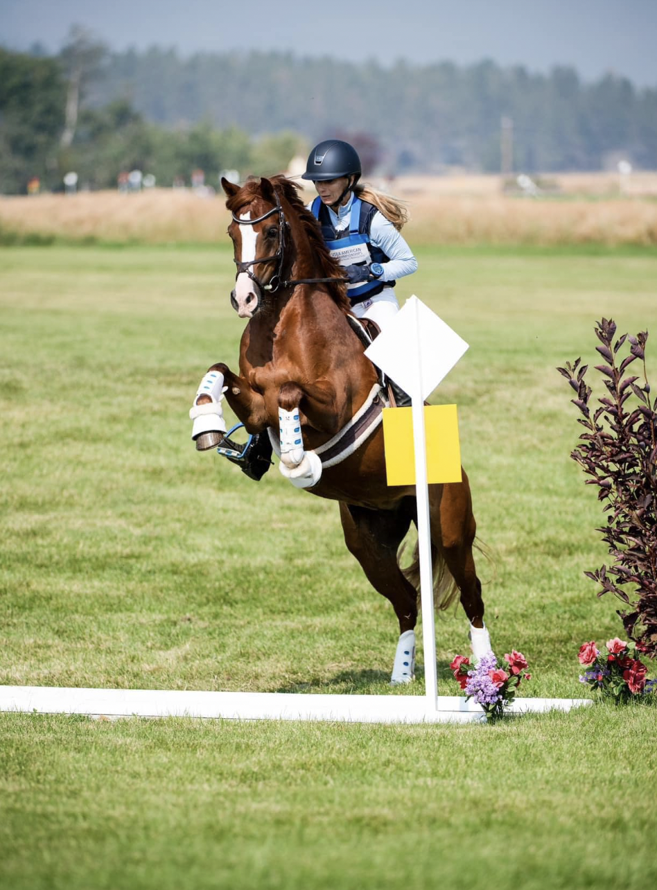 A female horse rider in a blue jacket and helmet competing in the cross-country phase , jumping over a ditch.