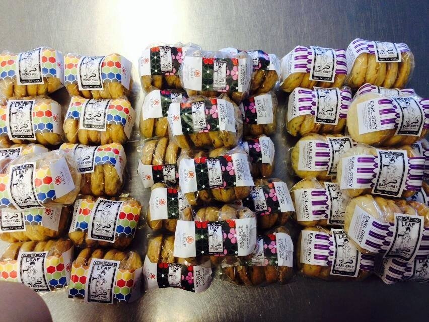 Several bags of Leaf Kitchen's cookies with various colorful labels and designs are arranged on a surface.