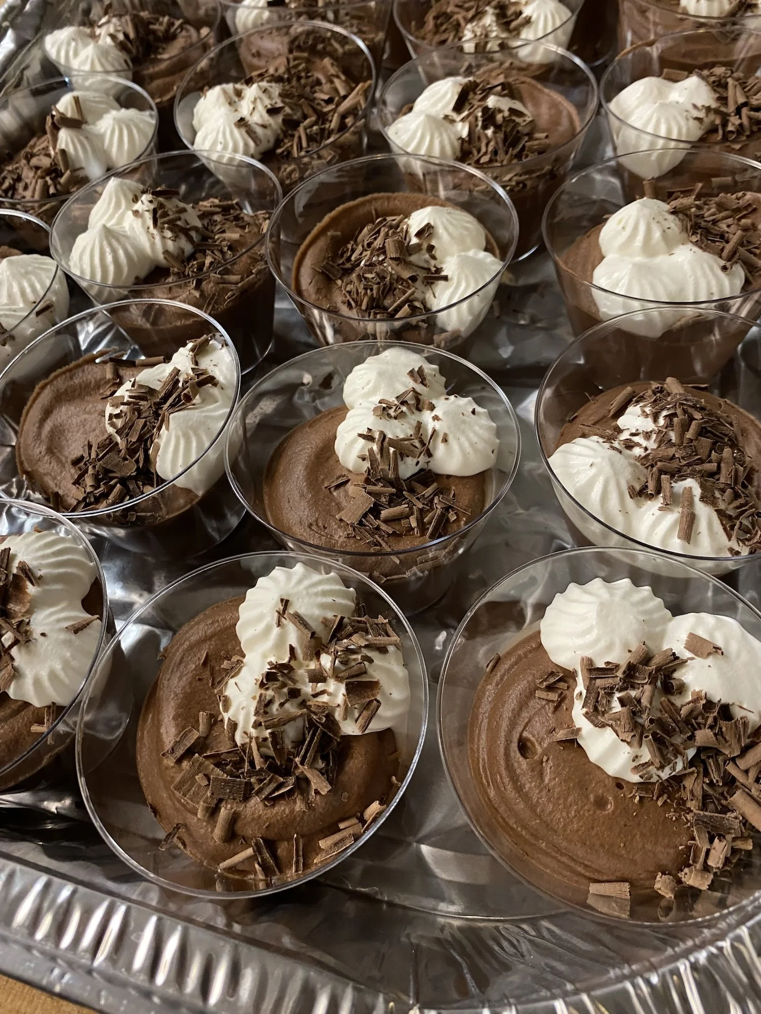 Multiple cups of chocolate mousse topped with whipped cream and chocolate shavings arranged on a tray at an event catered by Leaf Kitchen.