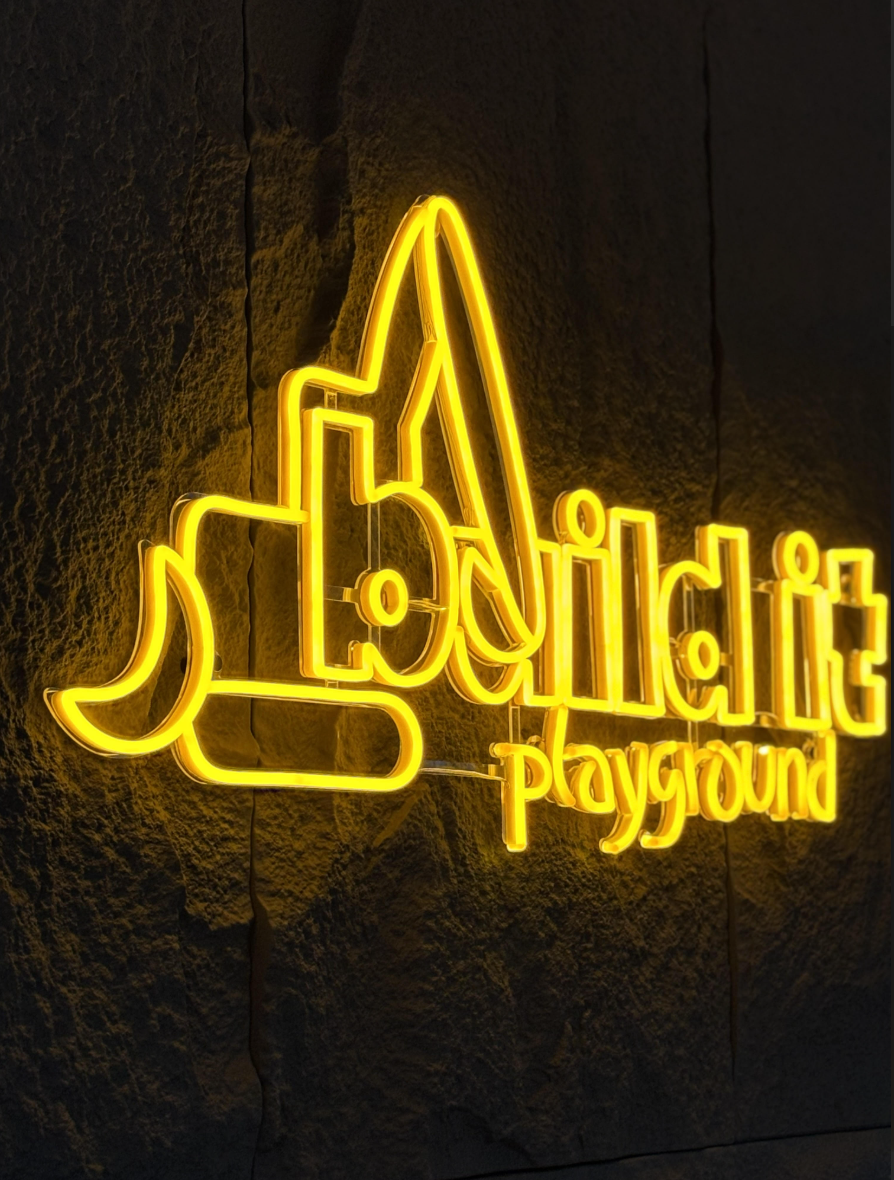 Neon sign reading 'Lavali PlayGround' with a moon and building silhouette, mounted on a dark textured wall.