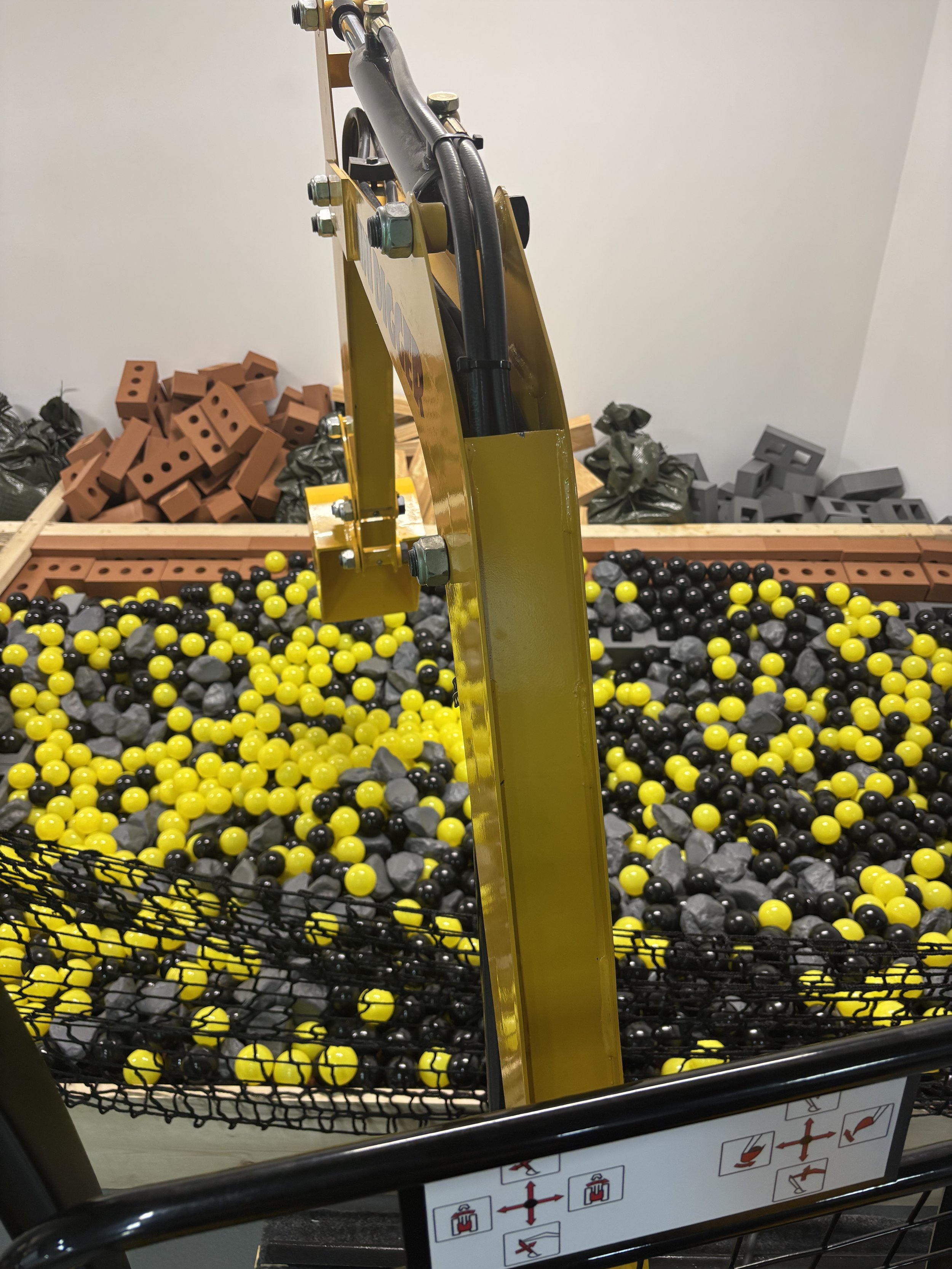 A shopping cart filled with yellow and black plastic balls, with a yellow vertical support and a warning label with instructions on the side of the cart.