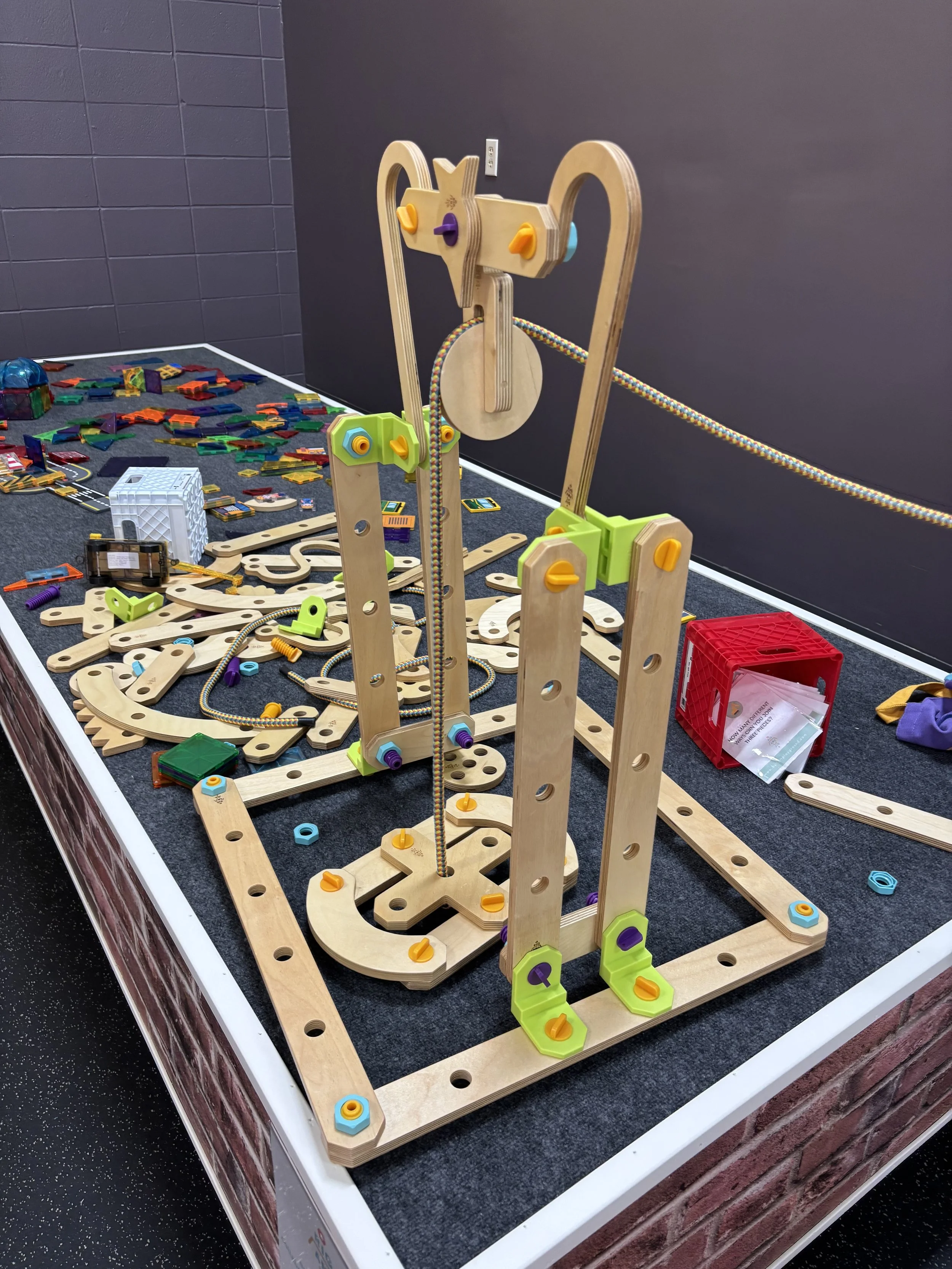 A marble run and construction toy setup on a table with wooden and plastic pieces, colorful tracks, and balls in a play area.