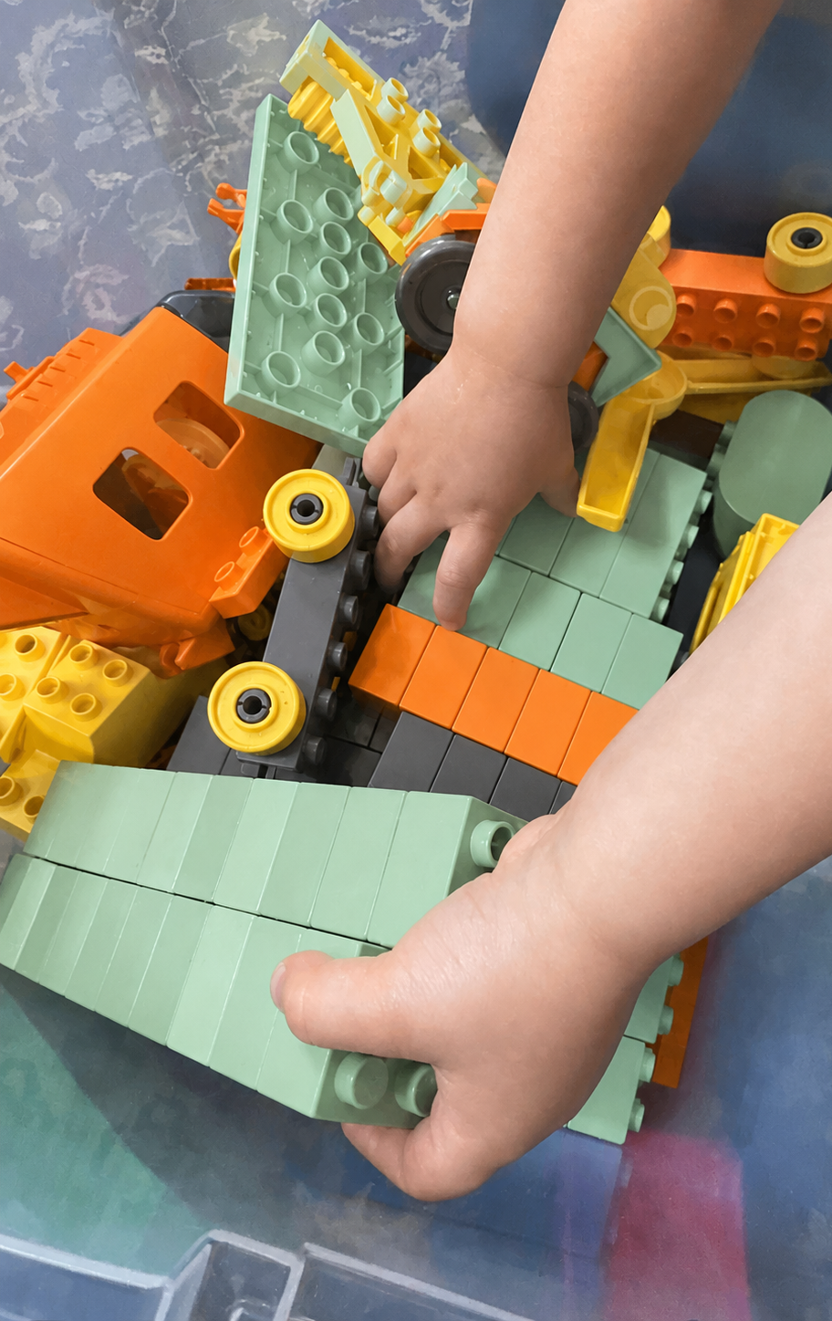 Child's hands playing with colorful plastic building blocks on a table.