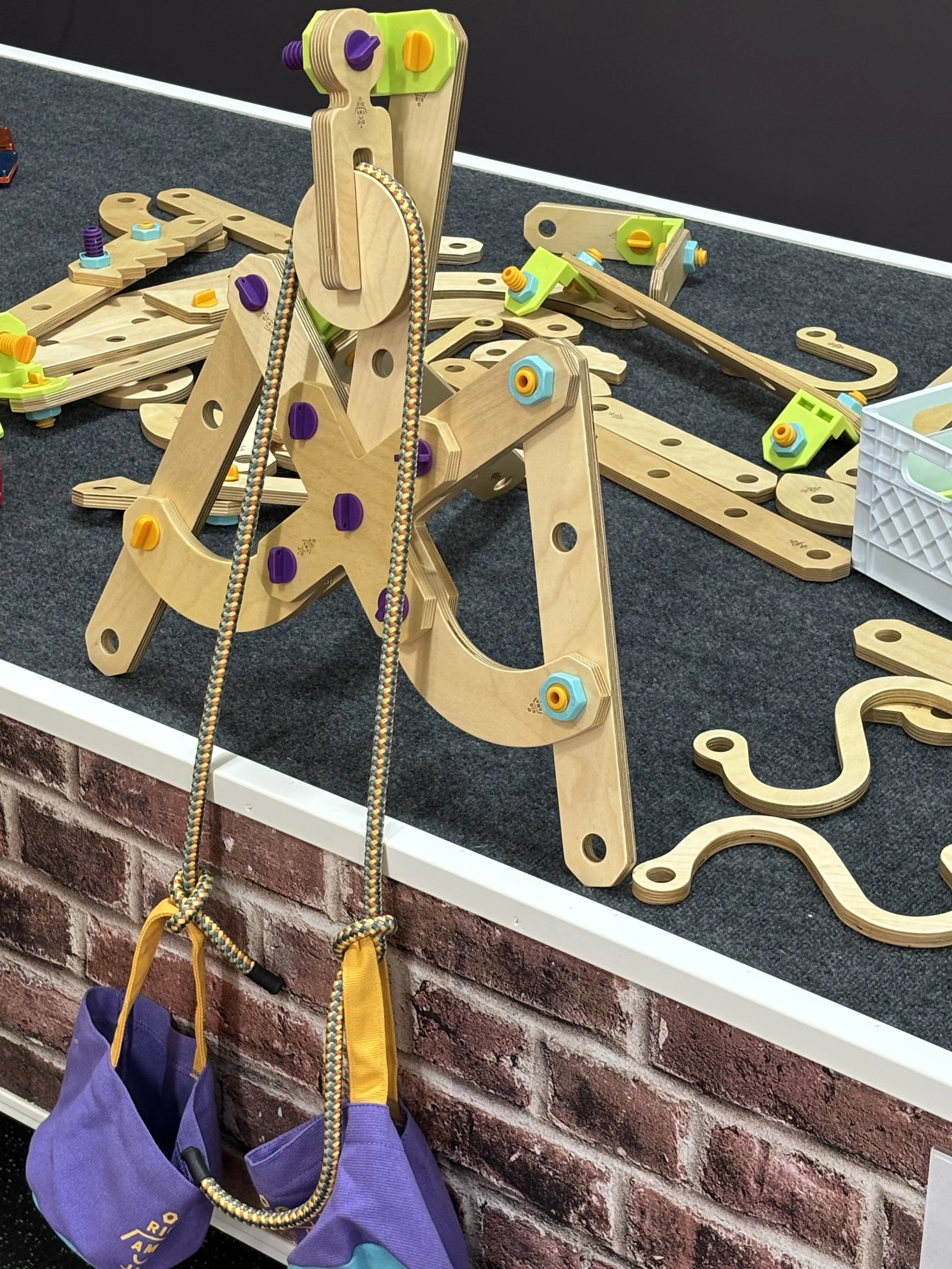 Colorful wooden toy construction set with various pieces and climbing accessories on a black carpeted table against a brick wall.