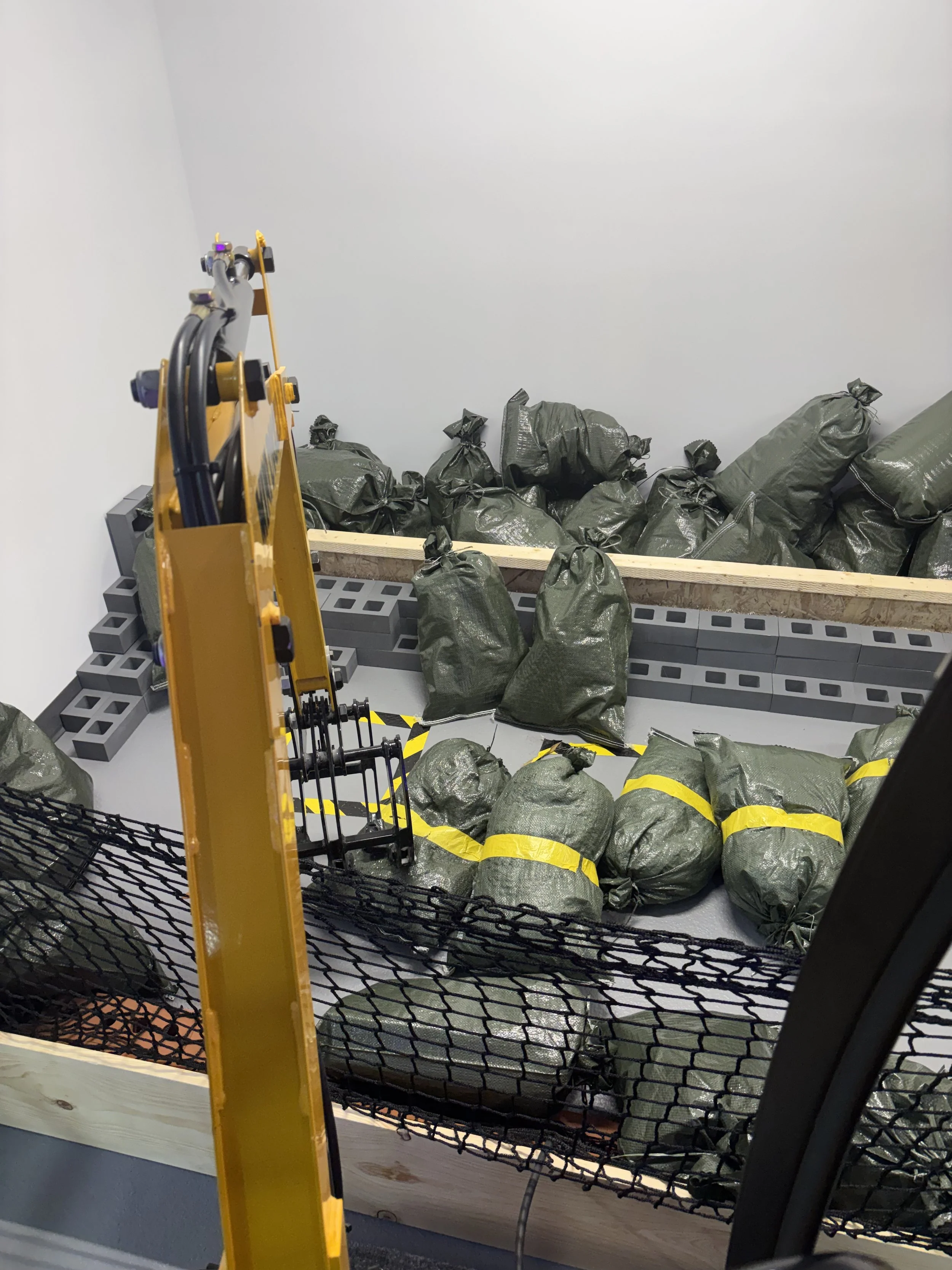 Room with a pile of green bags on a wooden platform, surrounded by safety barriers and construction equipment.