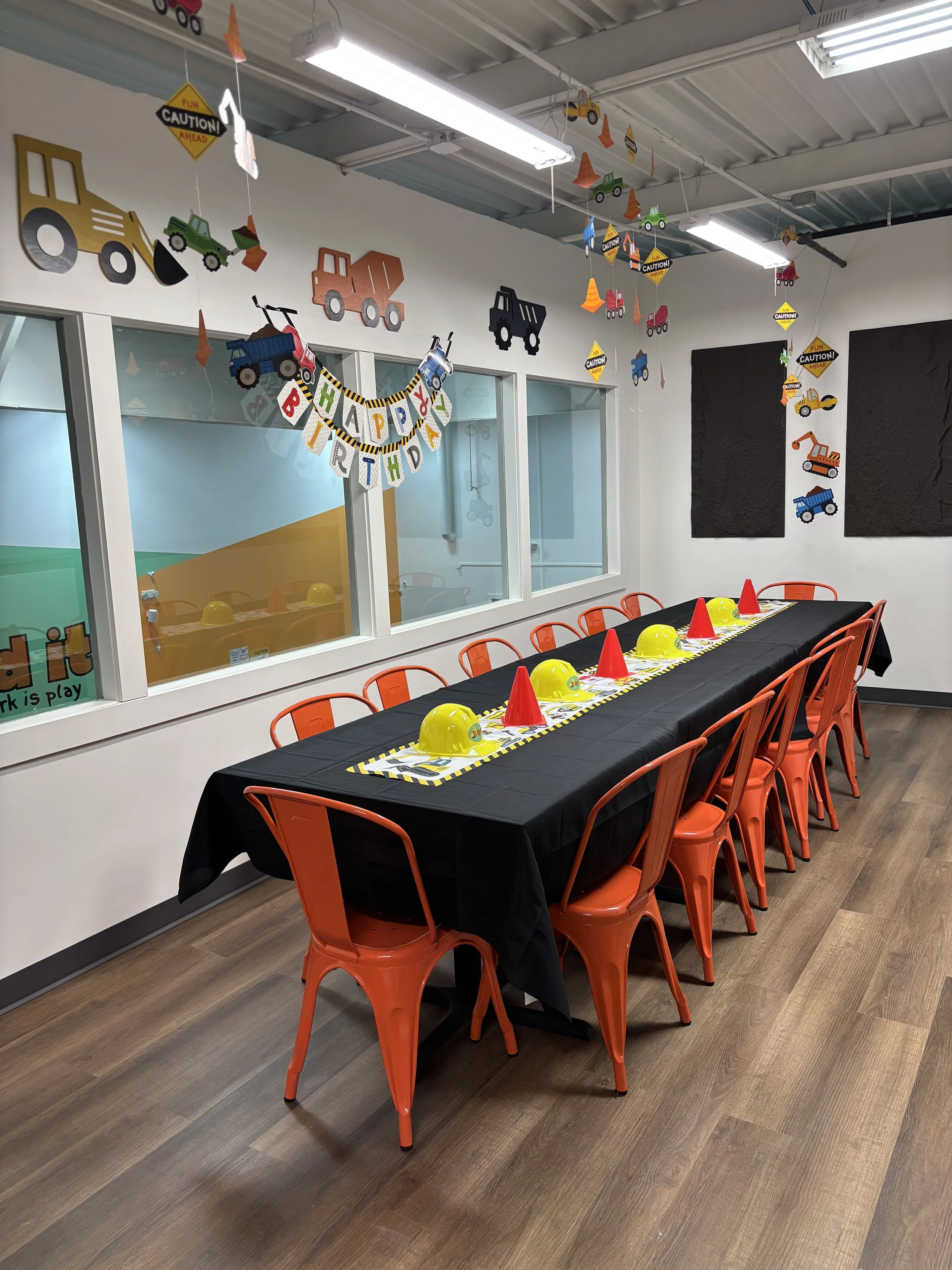 Party table decorated with construction-themed decorations, orange chairs, yellow construction helmets, and red traffic cones, set for a birthday celebration.