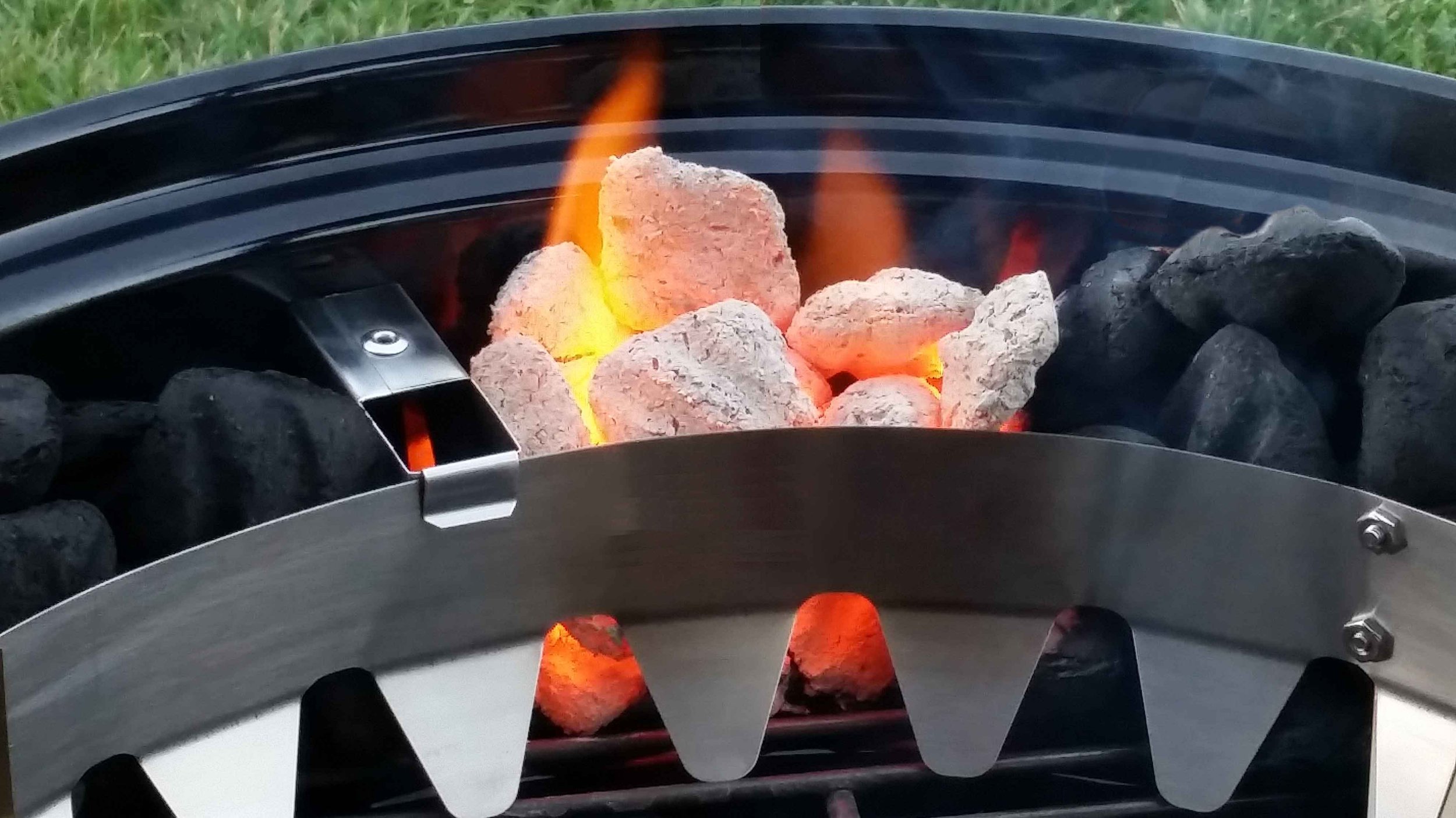 A close-up of a portable fire pit filled with rocks and glowing embers, with flames visible among the rocks.