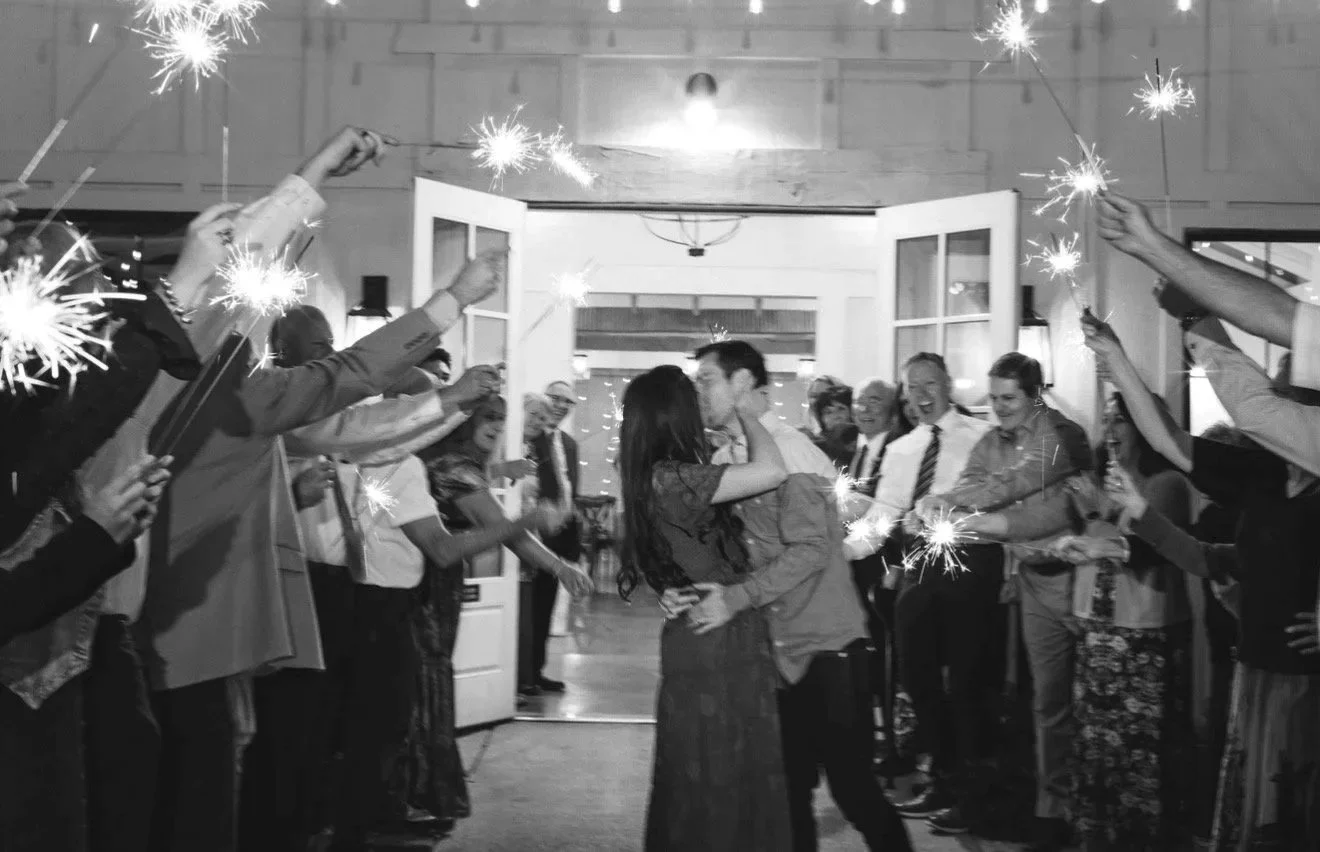 Photo by Sindy Mag Photo of a couple kissing in a doorway surrounded by family and friends in a sparklers send off taken in b&w motion blur.g of a couple kissing in a doorway