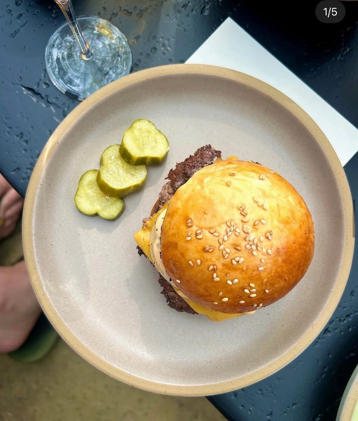 Bacon, cheese, and egg sandwich with a biscuit on top, served on a small bowl, with a dark mug of coffee or tea and a bottle of hot sauce in the background, all on a marble surface.