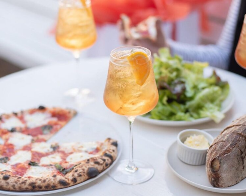 Table with a glass of peach iced tea, a pizza, a salad, a small dish of butter, and a loaf of bread.