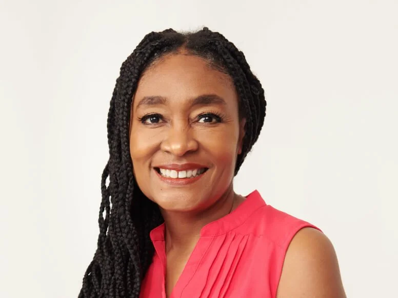 A smiling woman with braided hair wearing a sleeveless pink top against a light background.