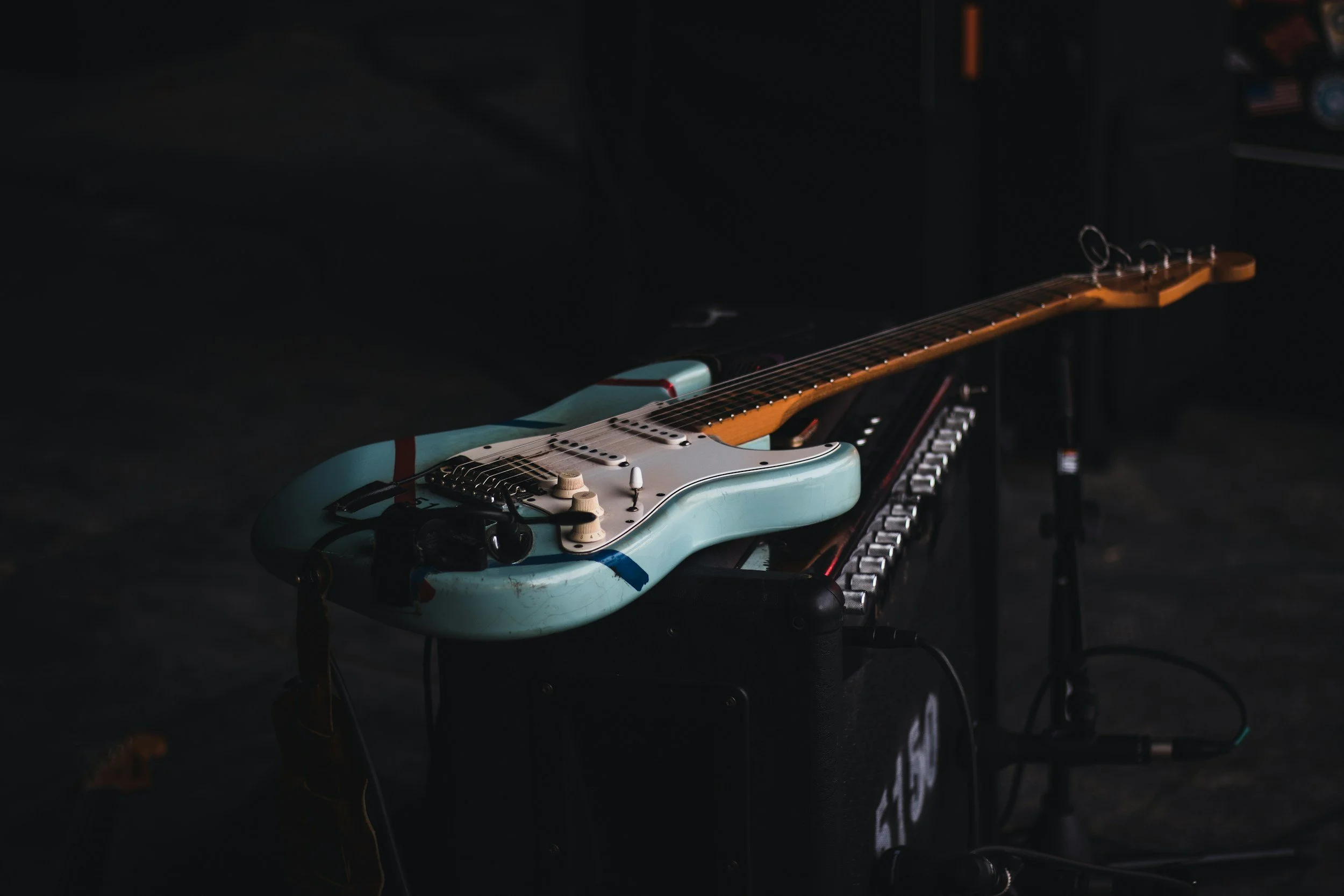 An electric guitar resting on a keyboard stand in a dimly lit room.