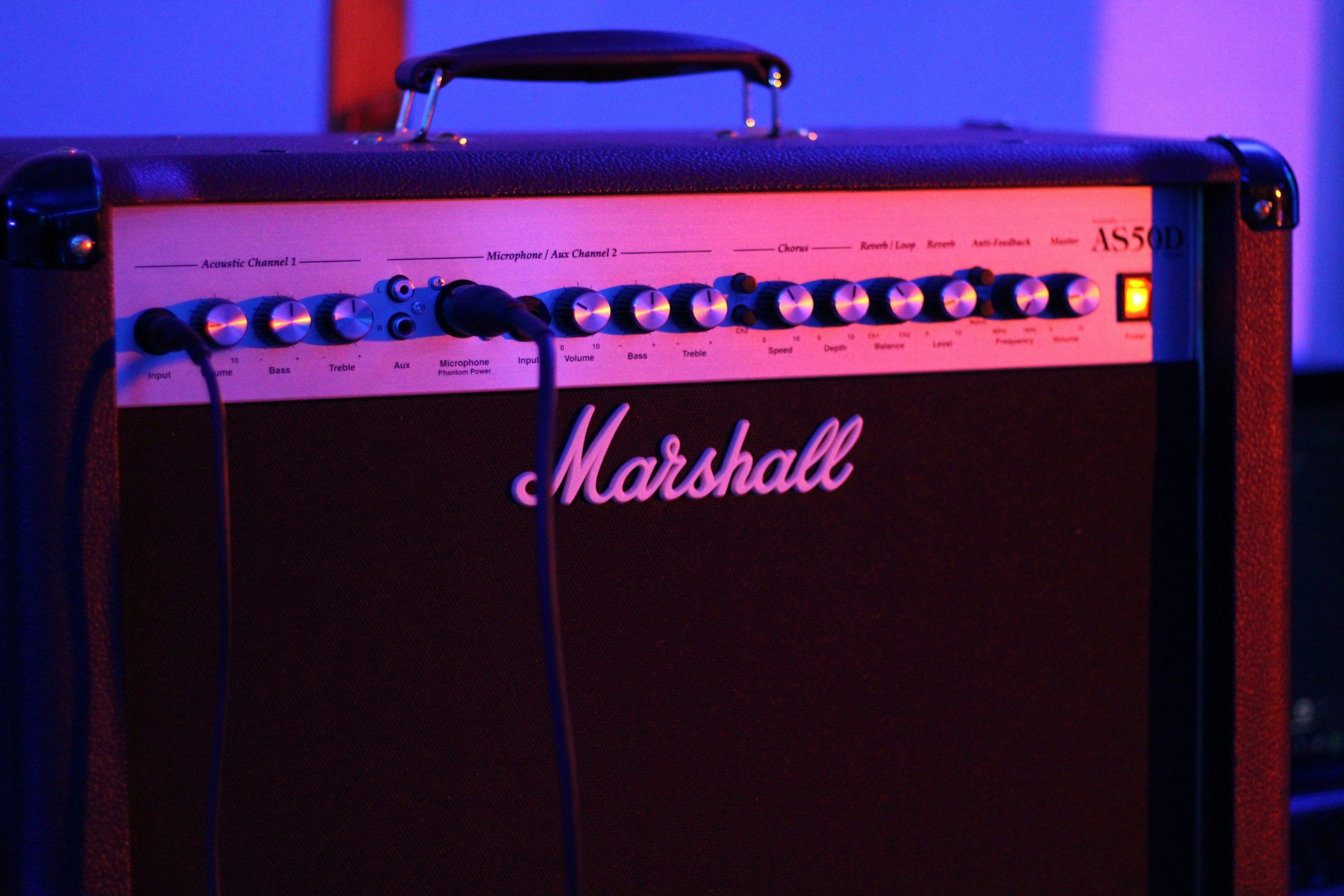 A Marshall guitar amplifier with a black speaker grill, control knobs on top, and a glowing orange power indicator light.