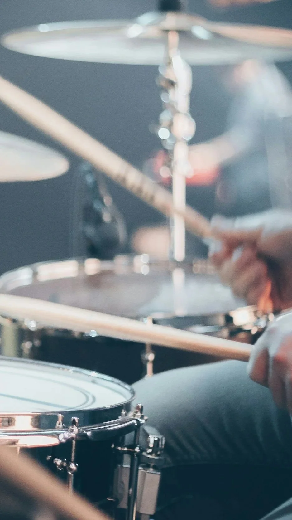 Close-up of a drummer playing a drum kit, showing drums, cymbals, drumsticks, and a person's hand in motion.