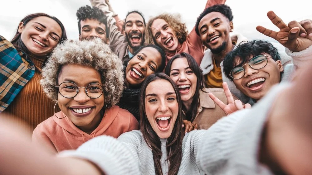 Group of diverse friends taking a selfie outdoors, smiling and making peace signs.