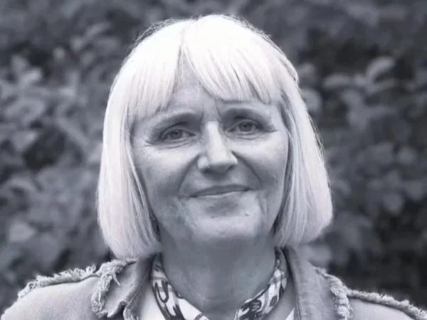 Black and white photo of a woman with shoulder-length hair smiling outdoors.