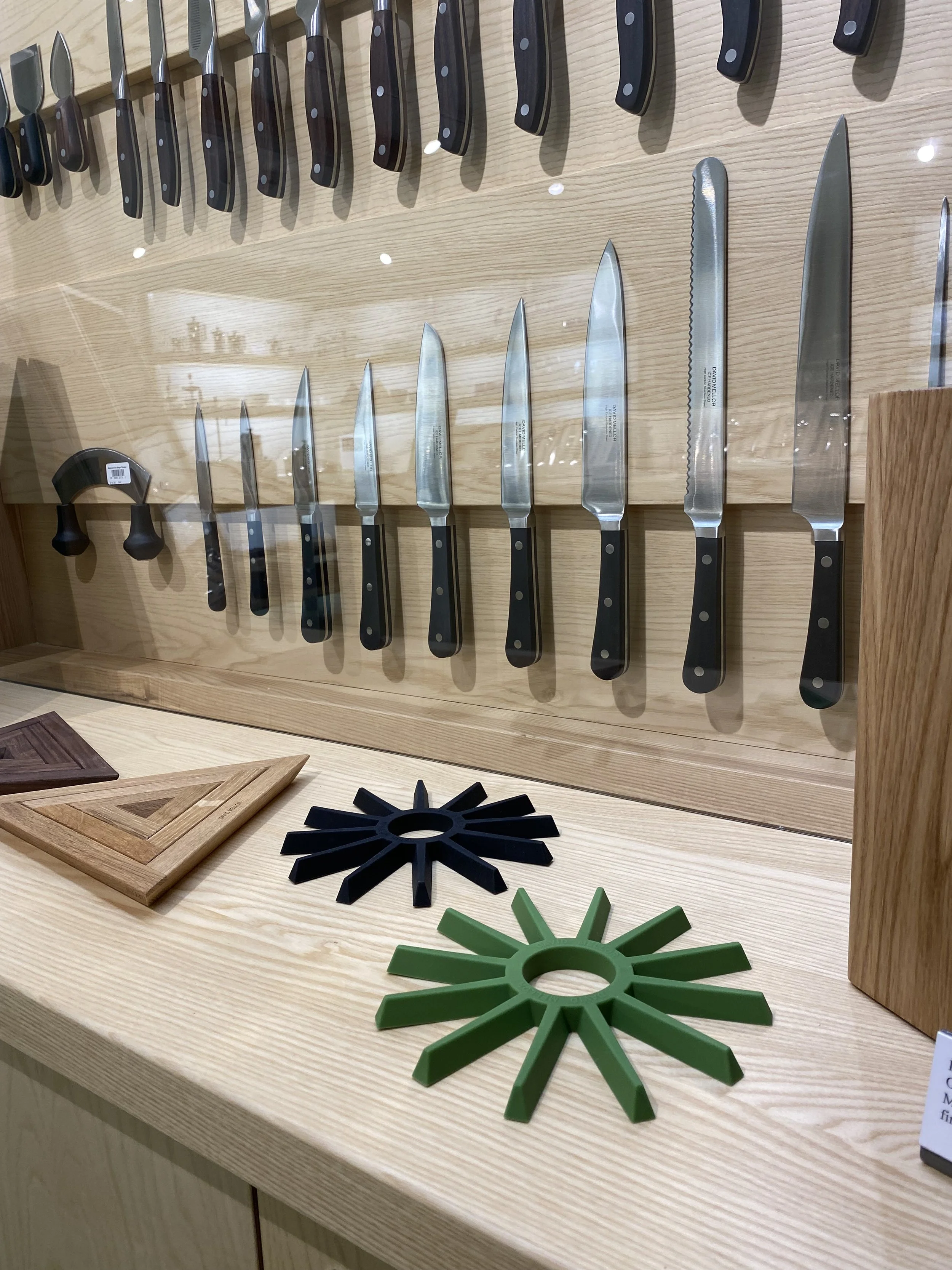 Display of various knives, cutting boards, and knife rests on a wooden surface.