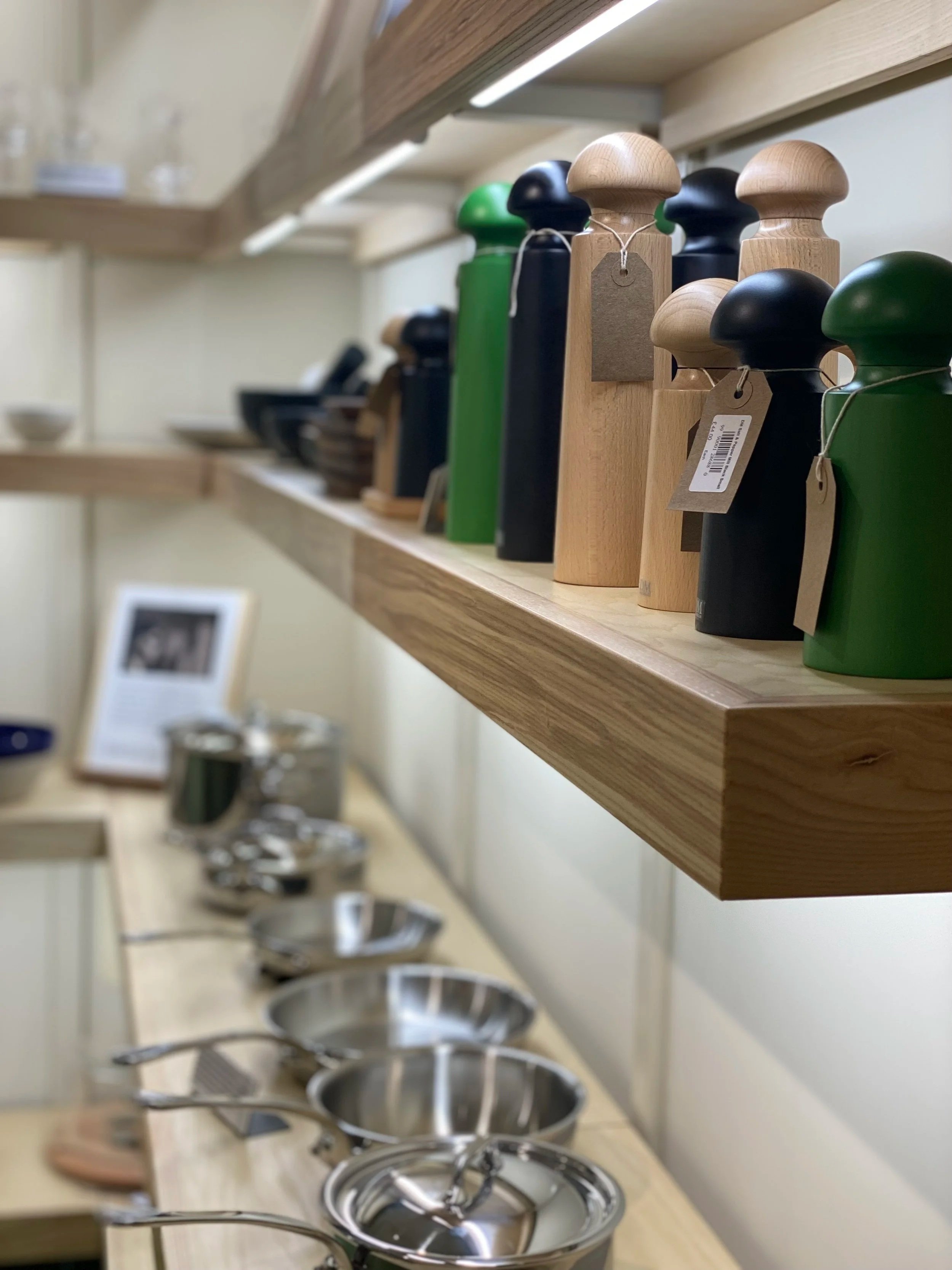 Wooden and green spice grinders on a wooden shelf, with stainless steel measuring cups and bowls below.