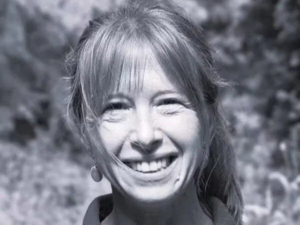 A woman smiling outdoors in black and white.