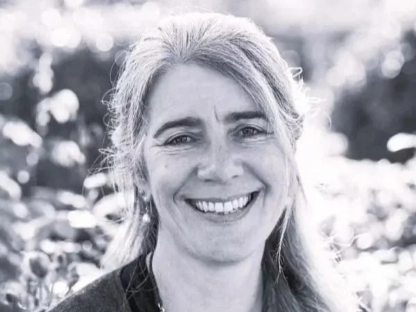 A smiling woman with long gray hair outdoors in a natural setting