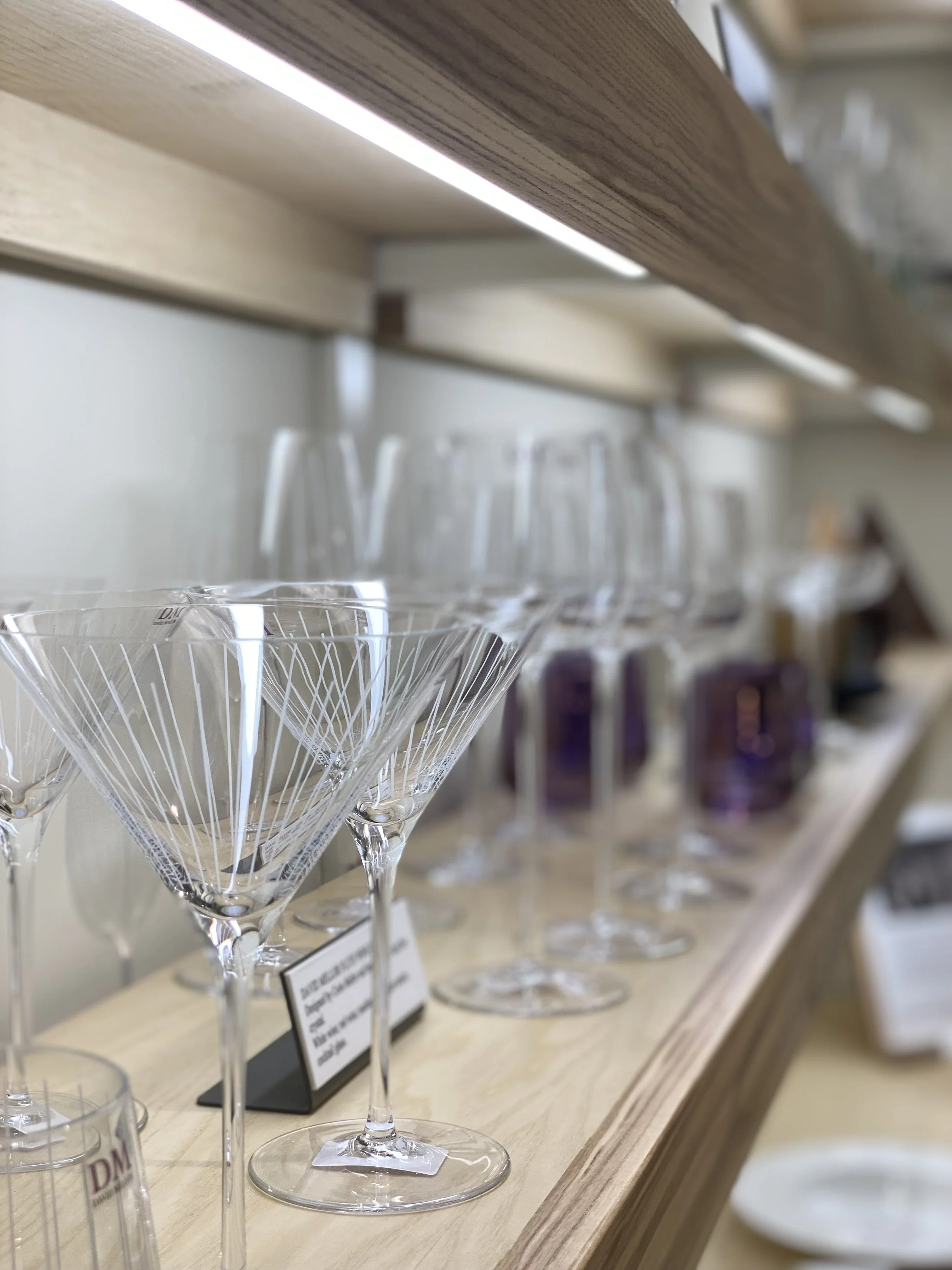 A display of various glassware, including martini glasses with a geometric pattern, arranged on a wooden shelf in a store.