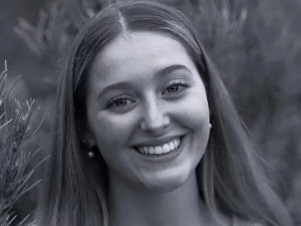 Black and white photo of a smiling young woman with long, straight hair outdoors.