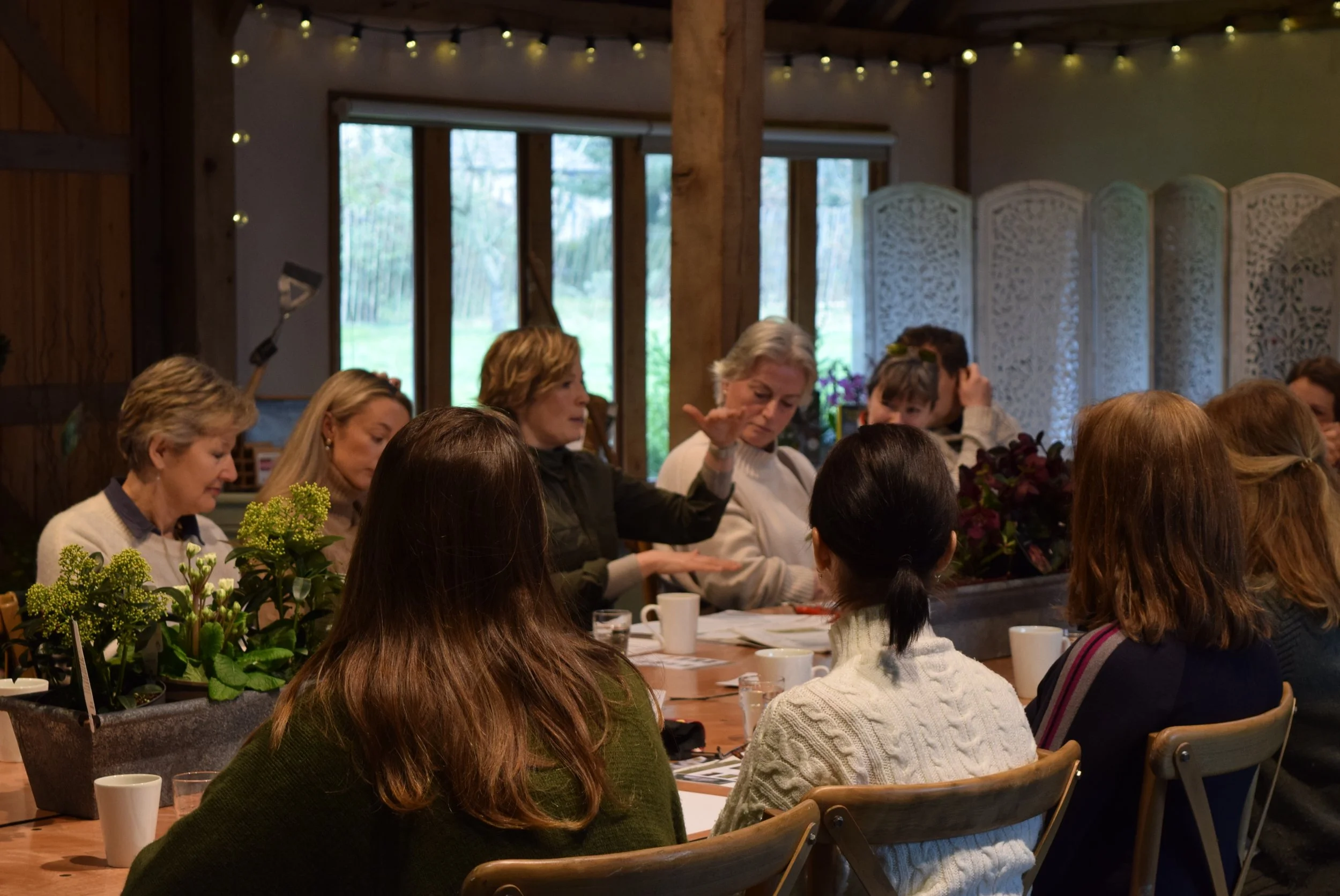 A group of women sitting around a wooden table in a cozy, listening to Kathy Slack in our events space, Orchard Barn, engaged in a discussion or meeting.