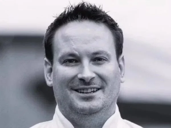 Black and white portrait of a smiling man with short dark hair, wearing a collared shirt.