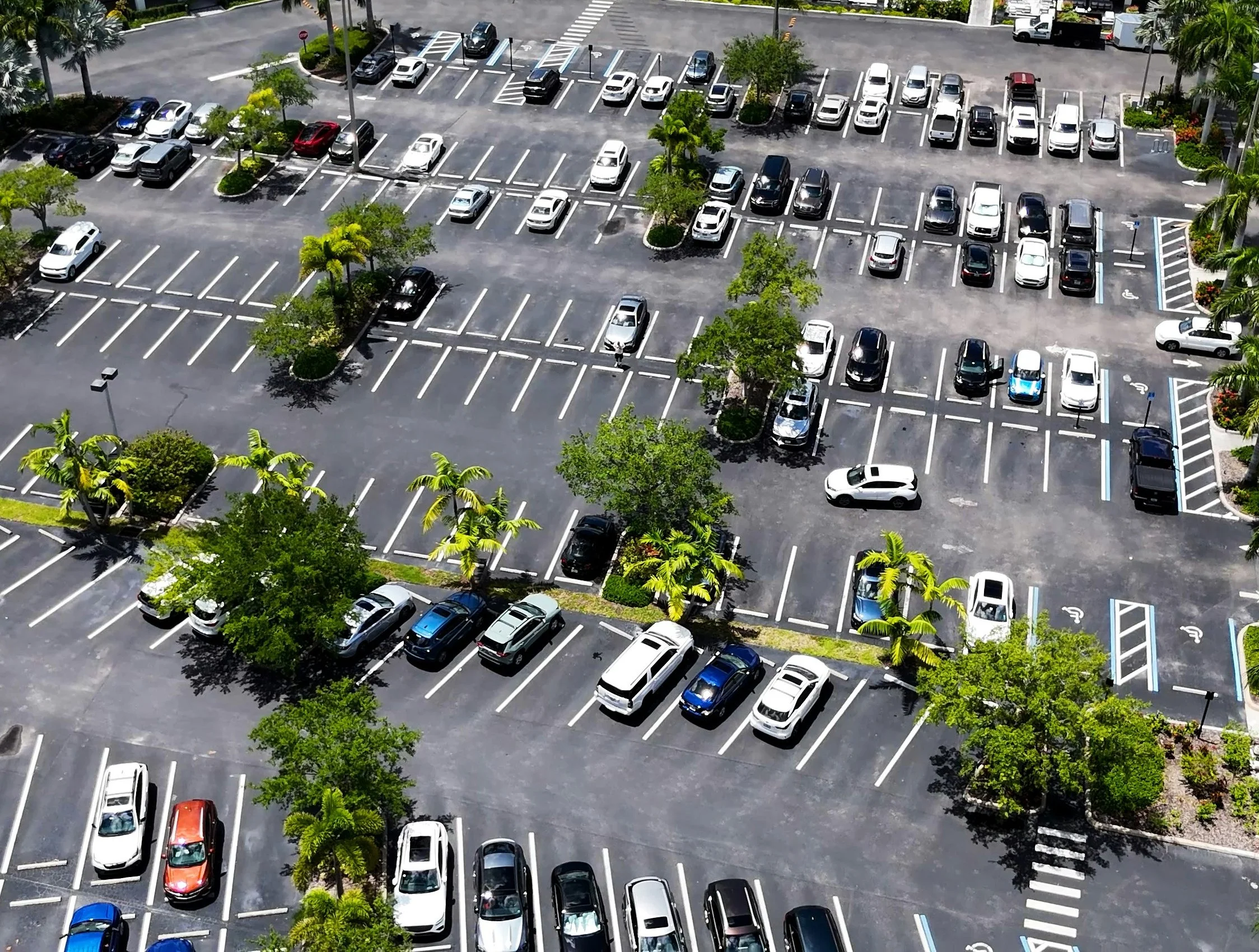 Aerial view of a mostly empty parking lot with some scattered vehicles and small trees