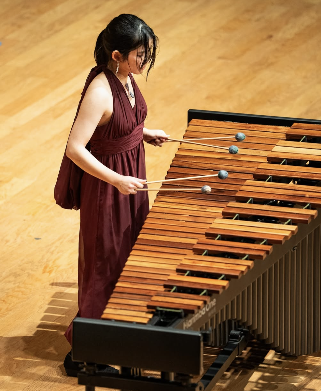A woman in a maroon dress playing a marimba with mallets during a performance.