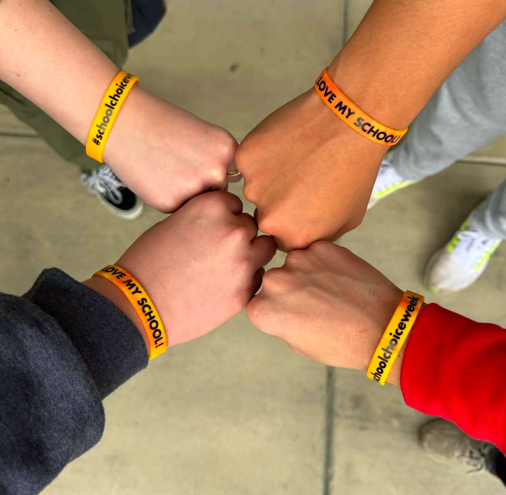 Four people forming a fist bump, each wearing colorful wristbands with school-related messages.