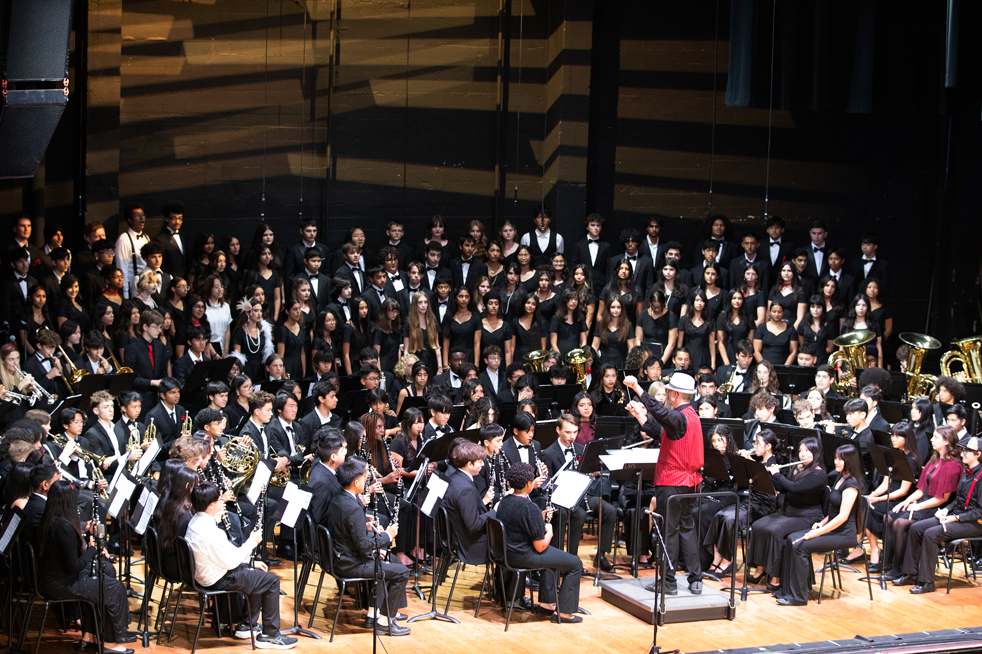 A large school orchestra performing on stage with students playing various instruments and a conductor leading them.
