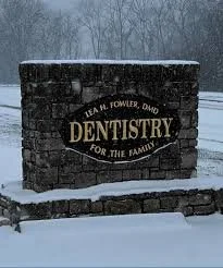 Signboard for a dentistry practice with a brick wall in a snowy outdoor setting.