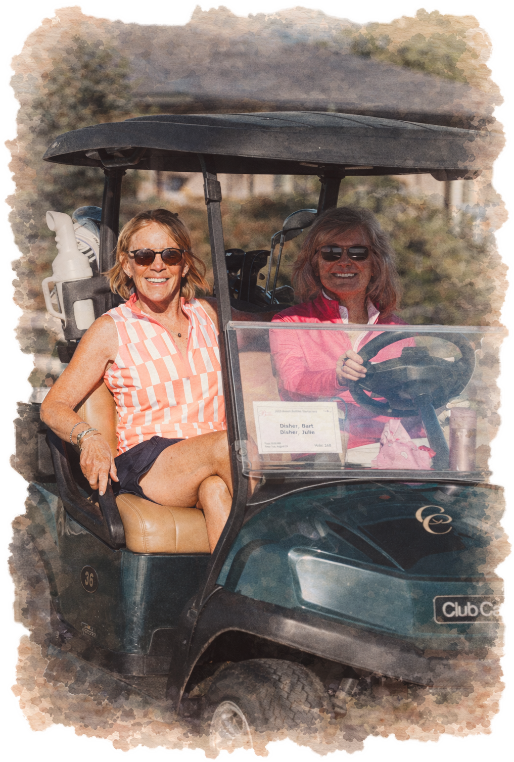 Two smiling women sitting in a golf cart on a sunny day, with one woman in the passenger seat and the other driving, surrounded by trees and outdoor scenery.
